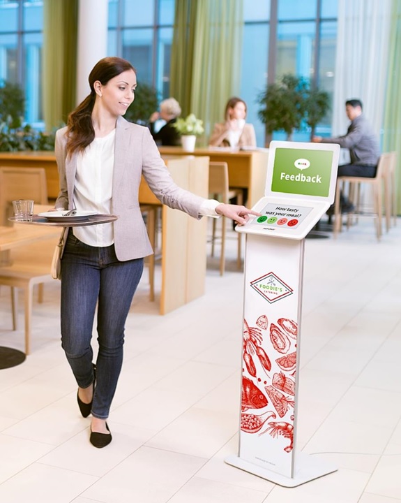 Eine Angestellte nutzt die Zufriedenheitsanalyse für die Gastronomie: sie geht am Zufriedenheitsmessgerät vorbei und beantwortet die Umfrage am Display.