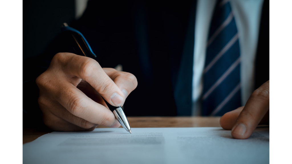Nahaufnahme von Händen einer Person die Stift in der Hand hält und einen Vertrag unterzeichnet