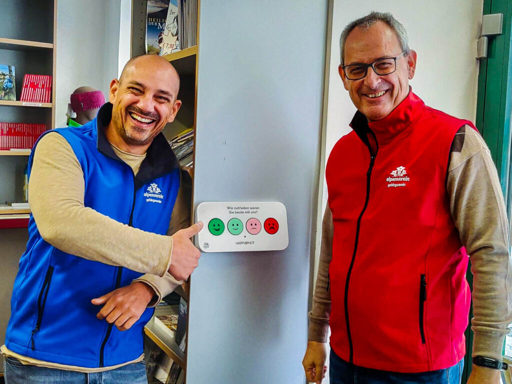 Der Vereinsmanager mit seinem Kollegen und dem HappyOrNot-Emoji-Terminal bei der Servicestelle des Alpenverein-Gebirgsvereins in Wien.