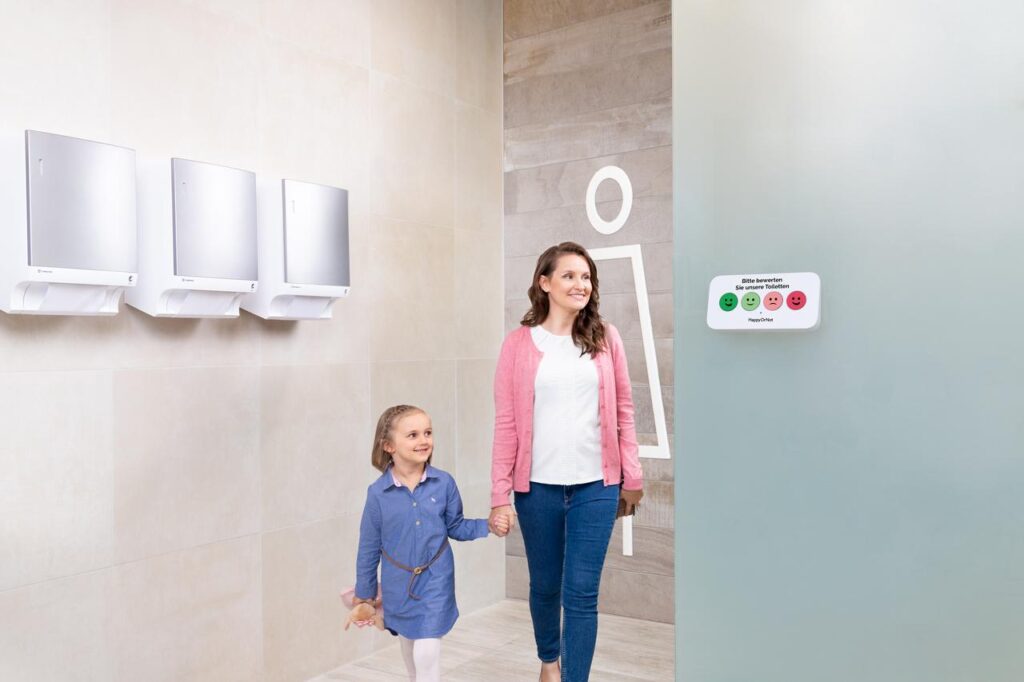 Messung der Zufriedenheit mit der Sauberkeit in einer Sanitäranlage mit HappyOrNot-Smiley Wall Terminal für die Nutzerinnen.
