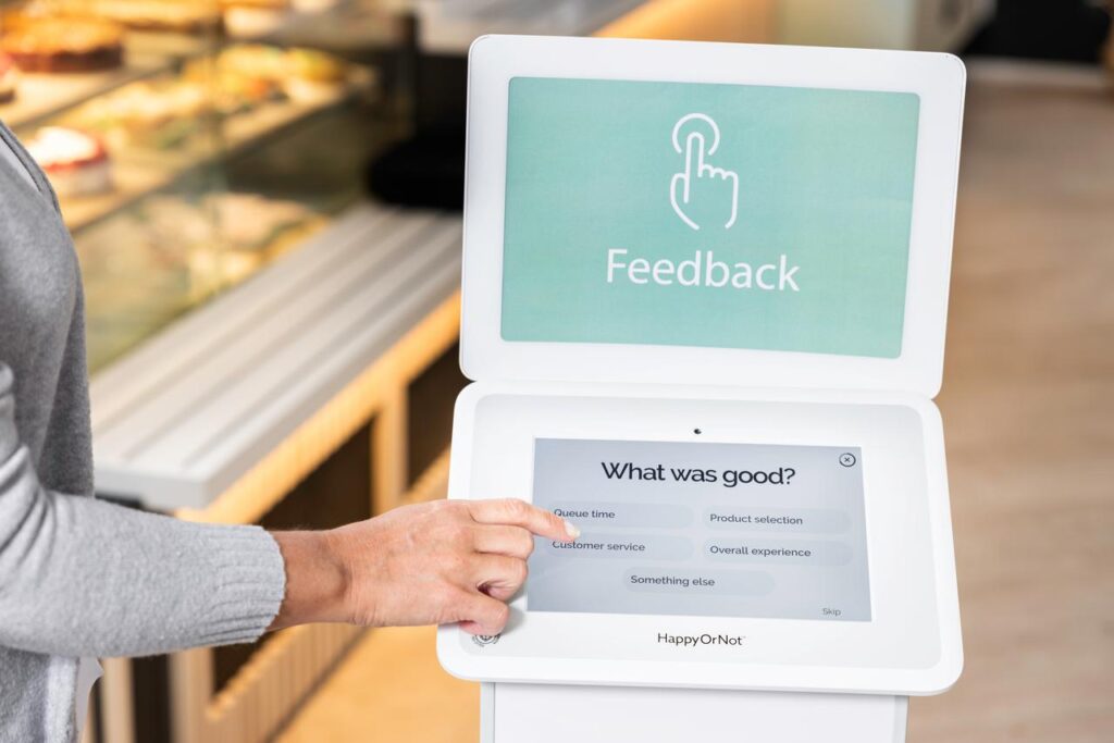 Praxisbeispiel aus der Retailbranche für den Einsatz eines Feedback-Kioskes. Eine Hand wählt die Kategorie "Kundenservice" als Grund für die Bewertung.