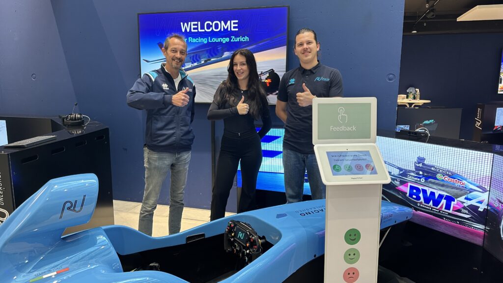 Ein Rennwagen-Simulator und das Team des Anbieters mit dem Smiley Touch Terminal im Vordergrund.